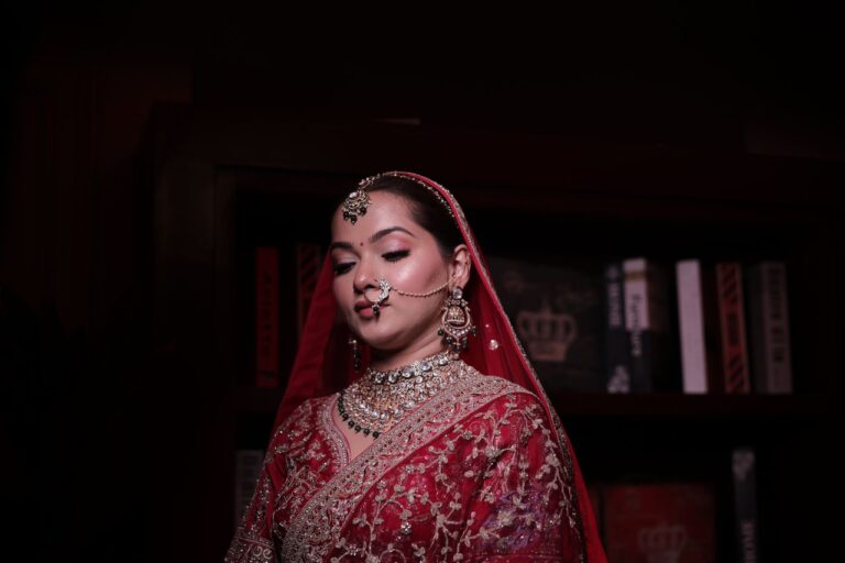 Elegant Indian bride in red sari with intricate jewelry, posing indoors.
